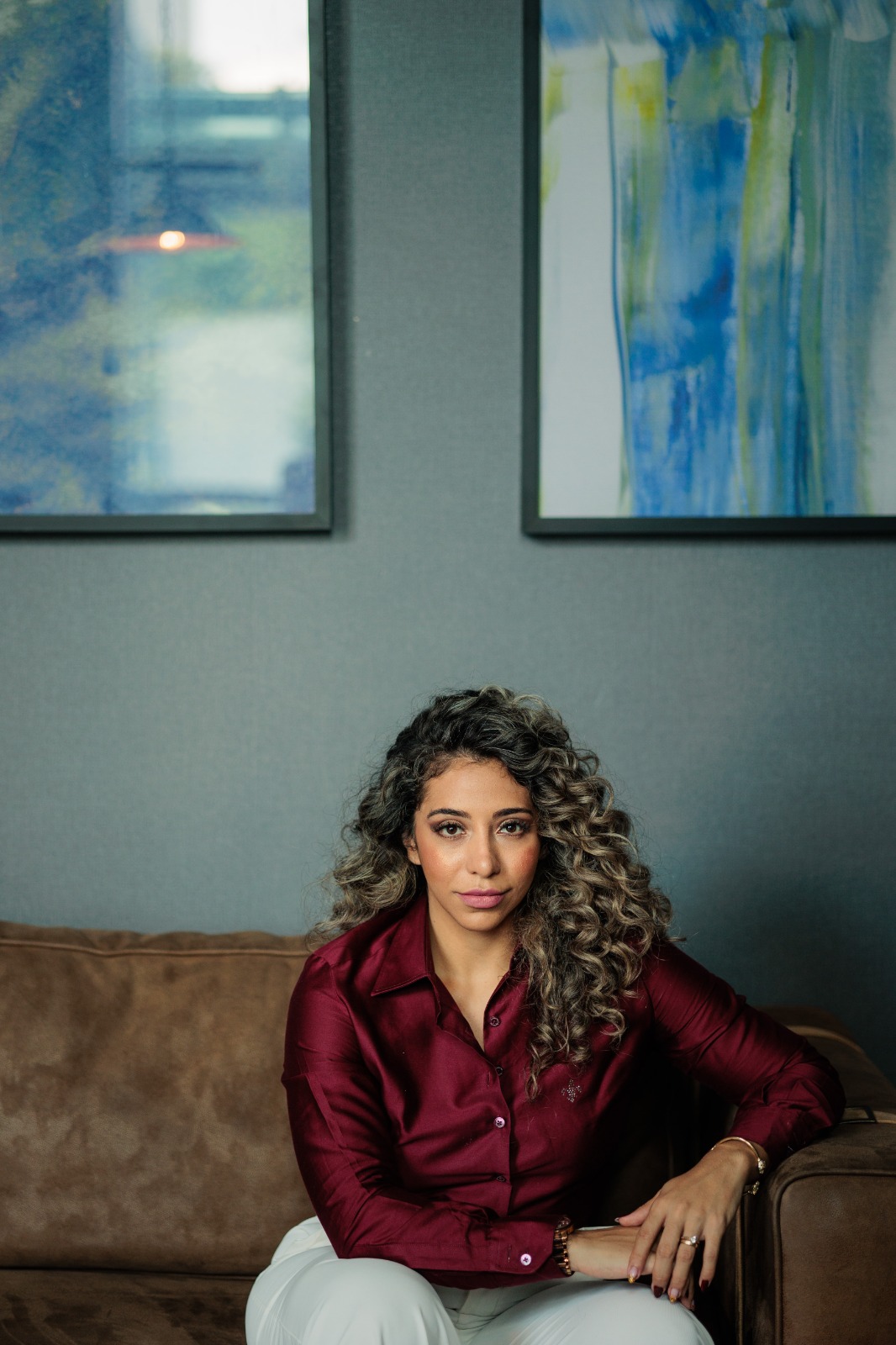 Stefany Rezende, de camisa bordô, sentada em um sofá em ambiente sóbrio com quadros ao fundo